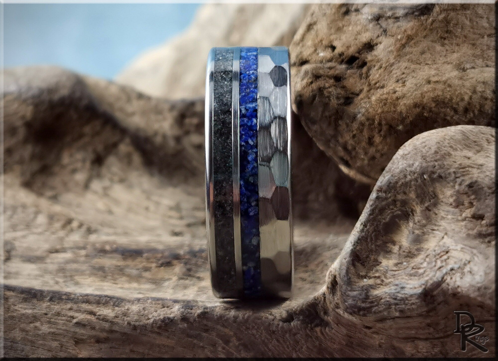 Hammered tungsten ring with two inlays featuring blue and black stone inlays on a textured surface