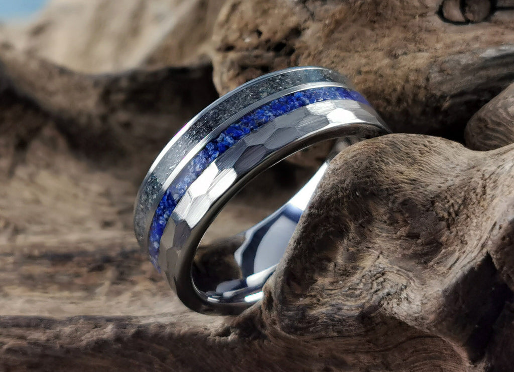Hammered tungsten ring with two inlays featuring blue and black stone details on wood background