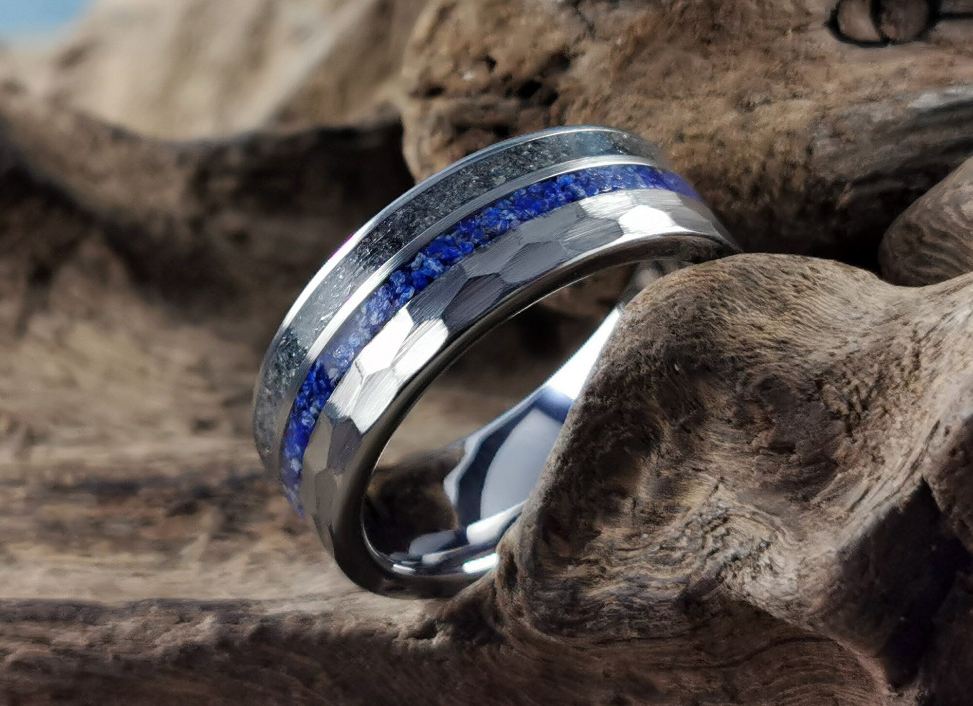 Hammered tungsten ring with two inlays featuring blue and black stone details on wood background