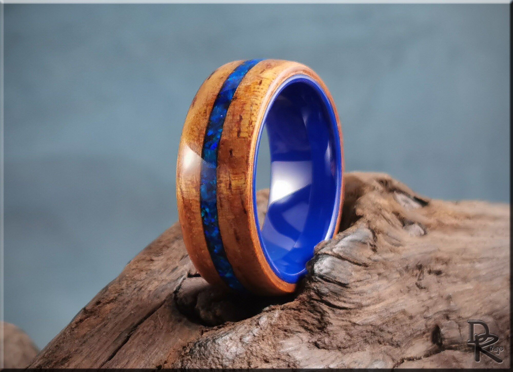 DR Rings koa wood ring with opal and ceramic blue interior on rustic wood background