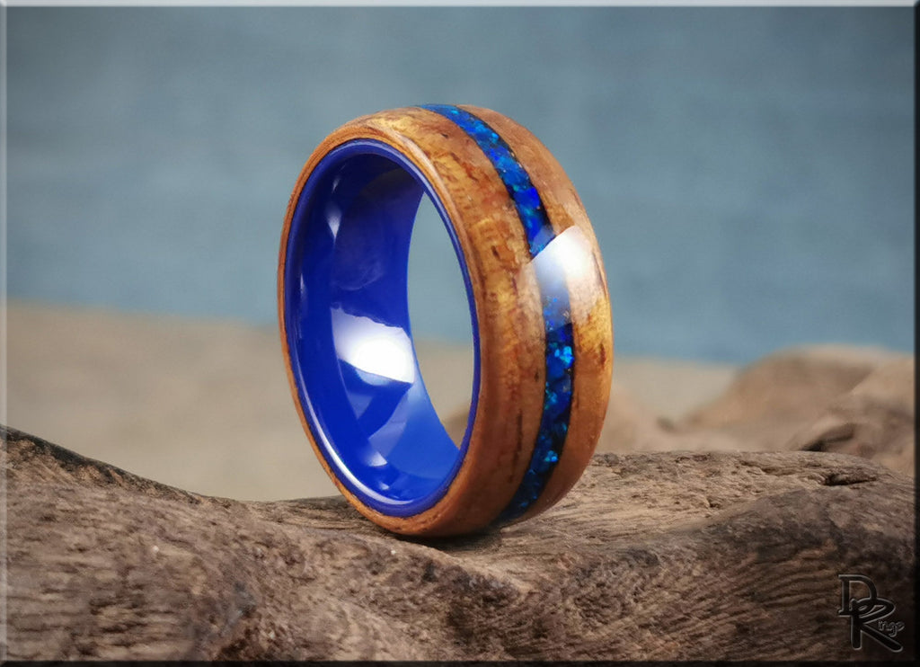 DR Rings koa wood ring with opal and ceramic blue inlay on driftwood background