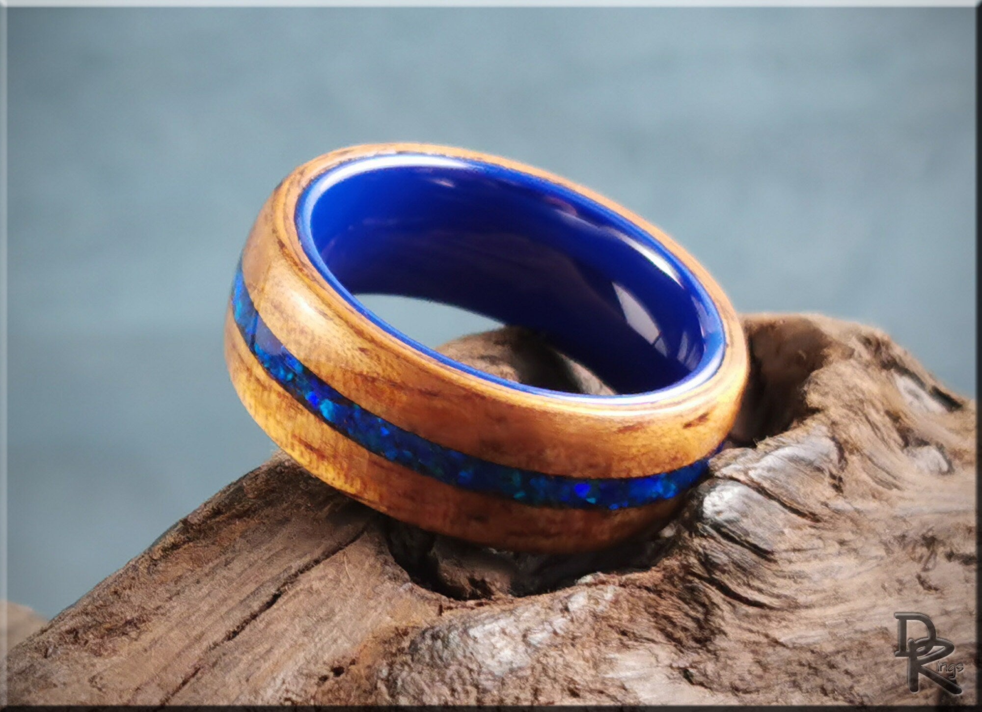 Koa wood ring with opal and ceramic blue inlay on natural wood background by DR Rings