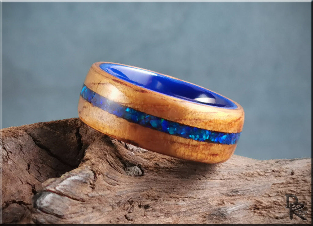 Koa wood ring with opal and ceramic blue inlay by DR Rings displayed on rustic wood