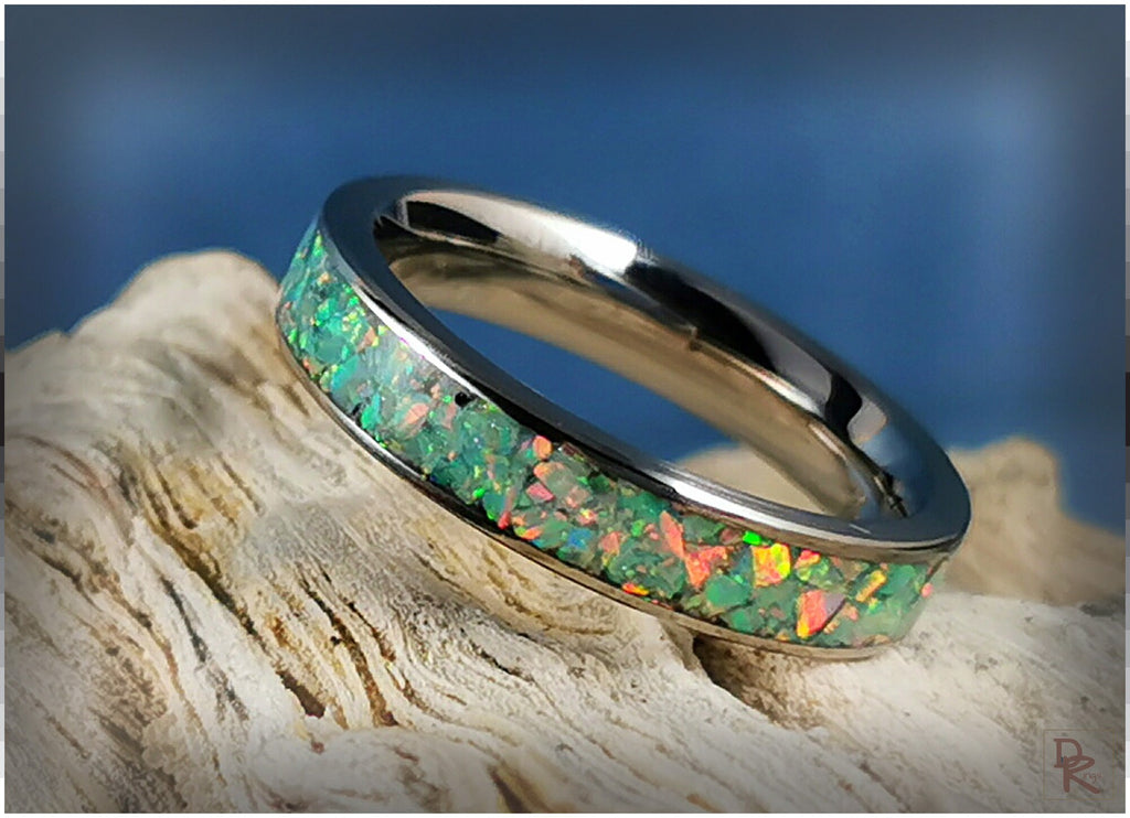 Narrow titanium ring with opal inlay showing vibrant green and orange colors on textured surface