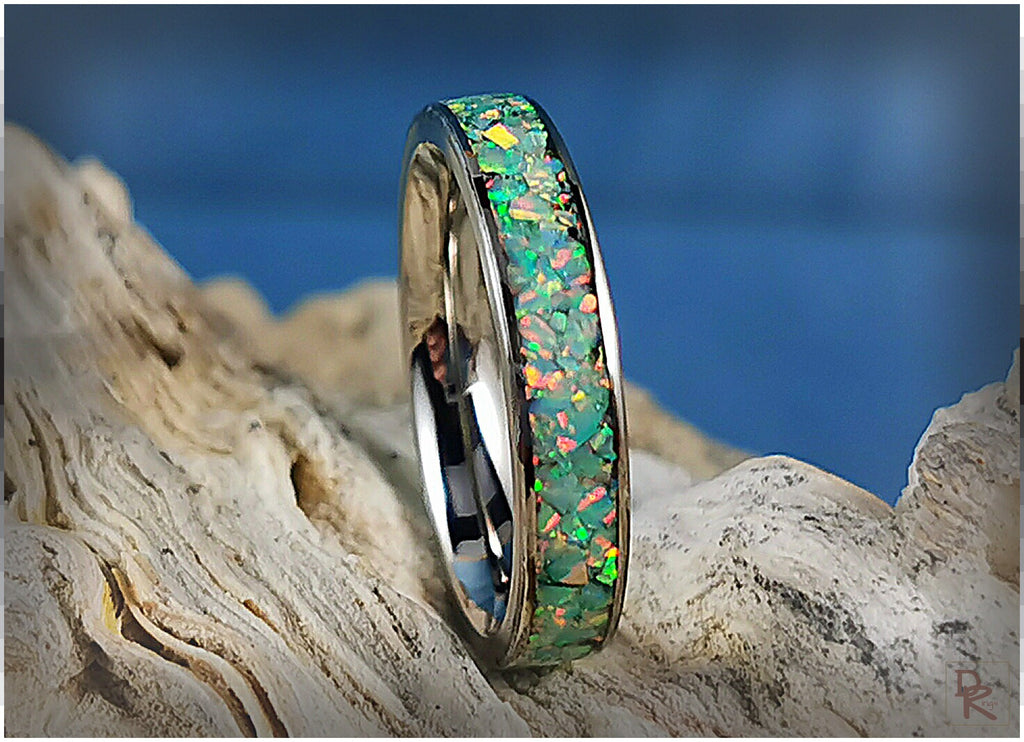 Narrow titanium ring with opal inlay displaying colorful iridescent fragments on natural wood