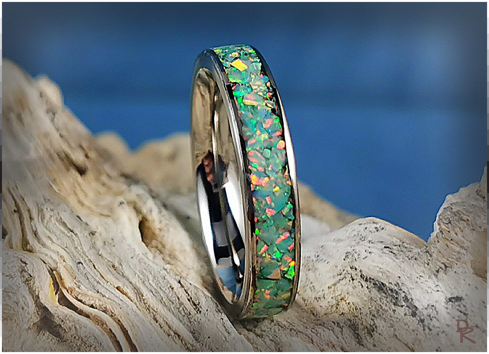 Narrow titanium ring with opal inlay displaying colorful iridescent fragments on natural wood