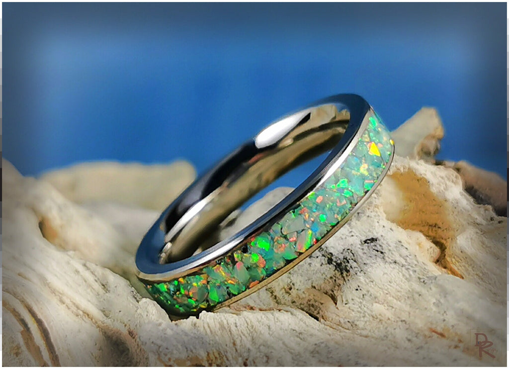 Narrow titanium ring with opal inlay featuring vibrant green and yellow hues on textured background
