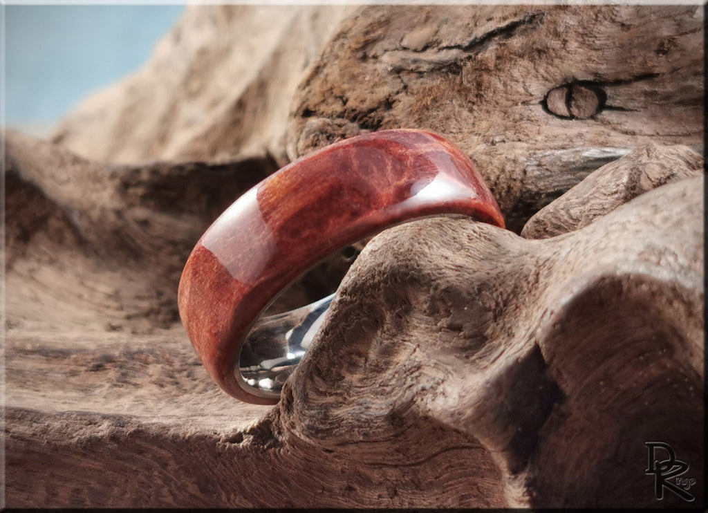 Close-up of a redwood ring on titanium resting on textured wood background by DR Rings