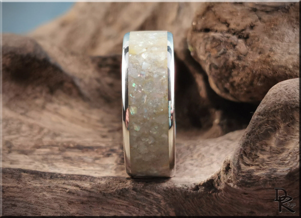 Sterling silver ring with pearl inlay displayed on textured wood surface by DR Rings