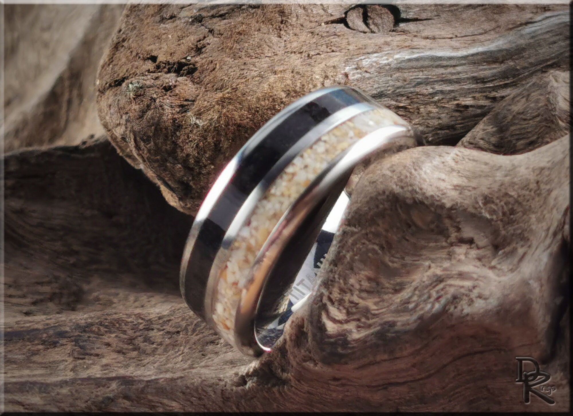 DR Rings titanium ring with dual sand inlays resting on rustic driftwood background