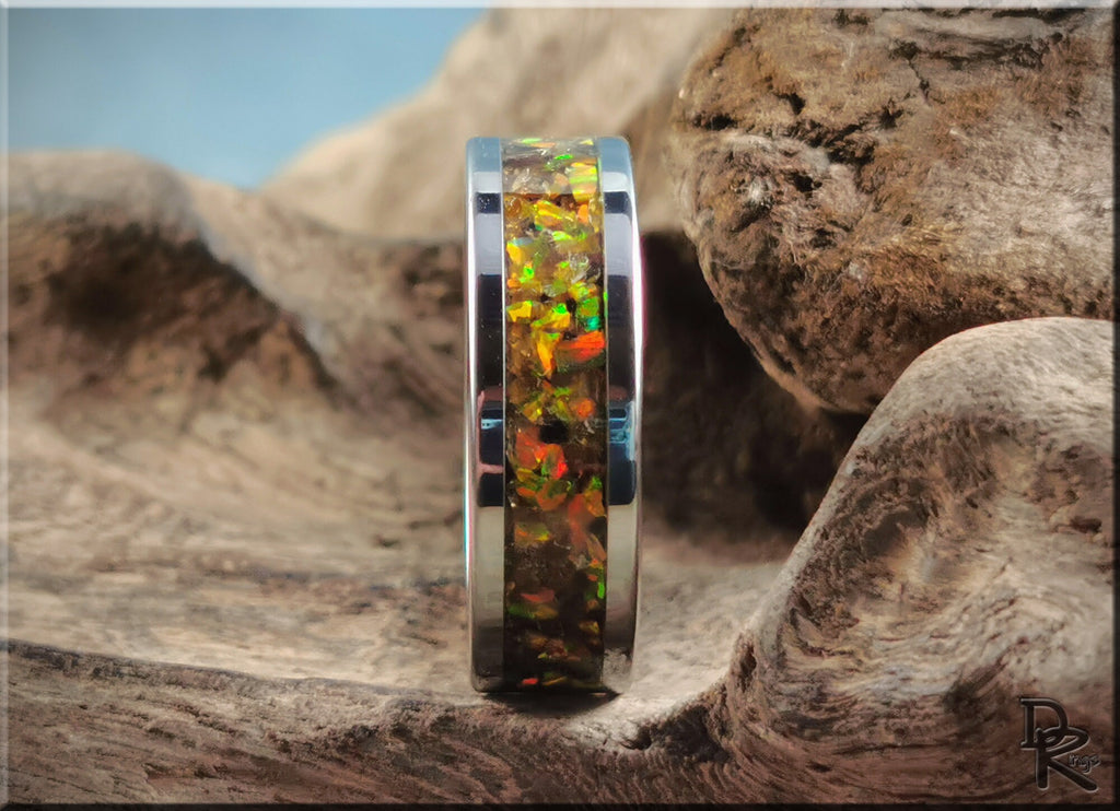 DR Rings titanium ring with inlay featuring iridescent orange and green opal design on rustic wood background