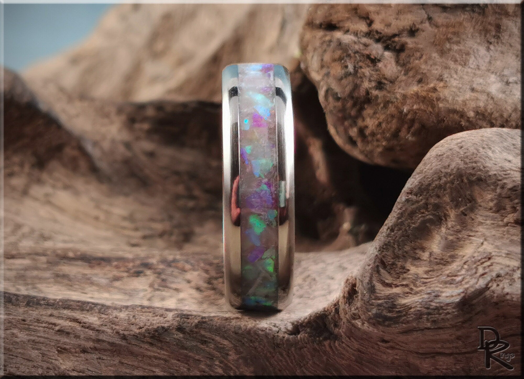 DR Rings titanium ring with inlay featuring colorful opal design set against rustic wood background