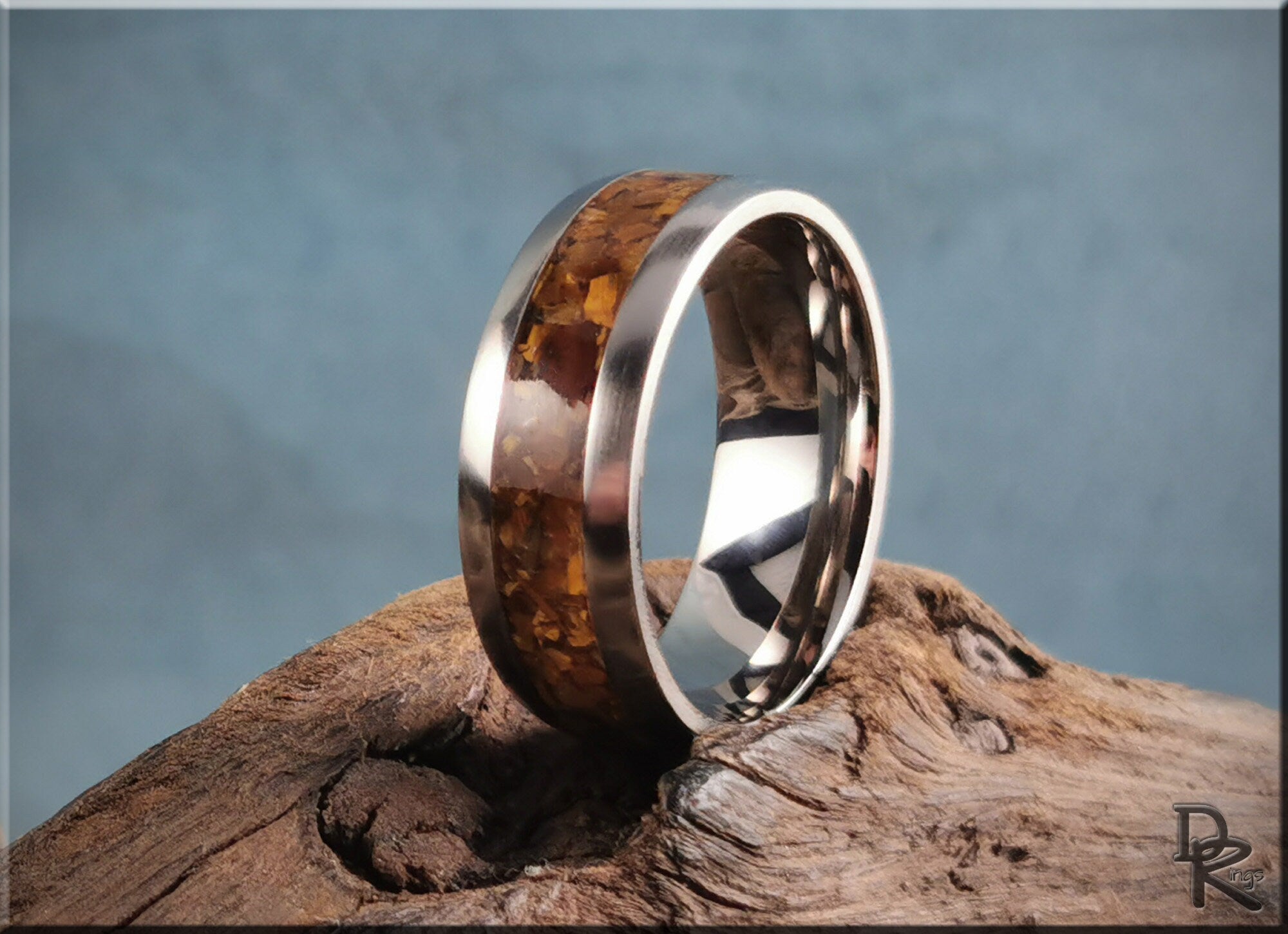 DR Rings titanium ring with inlay featuring polished metal band and amber wood inlay on rustic wood surface