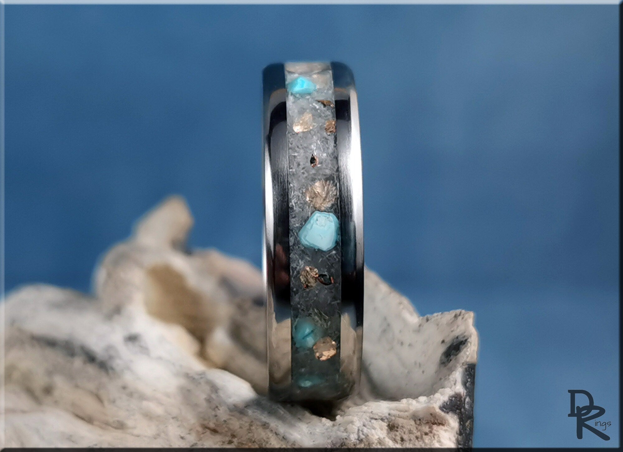 DR Rings titanium ring with inlay featuring blue and metallic accents on a textured background