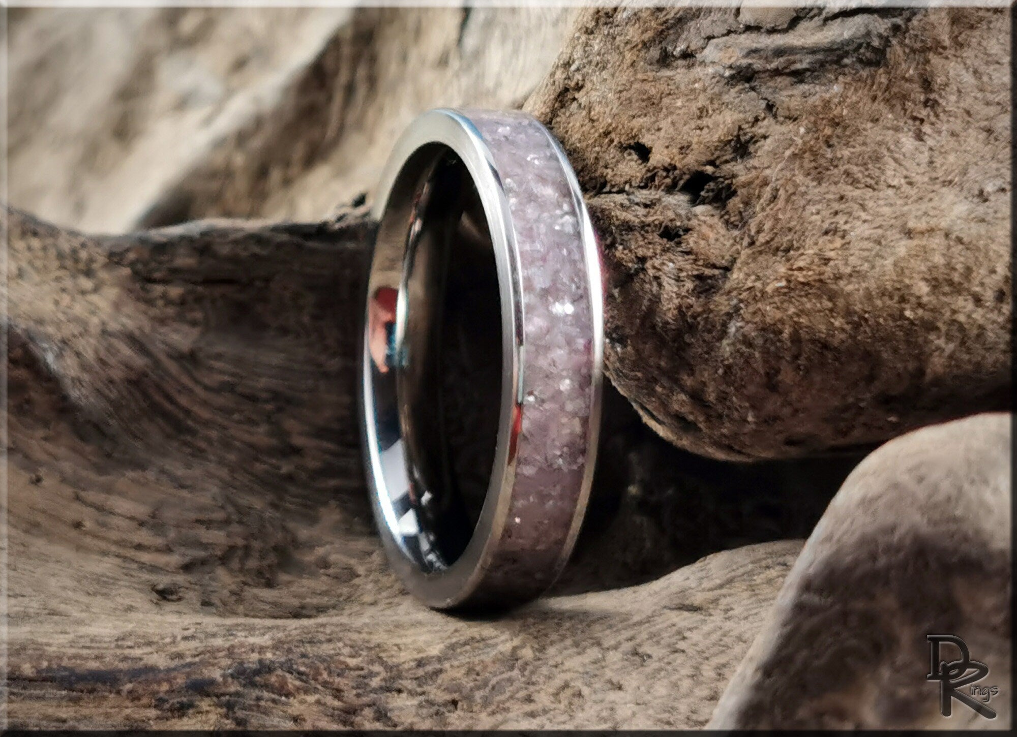 Close-up of a titanium ring with lepidolite inlay resting on natural textured wood background