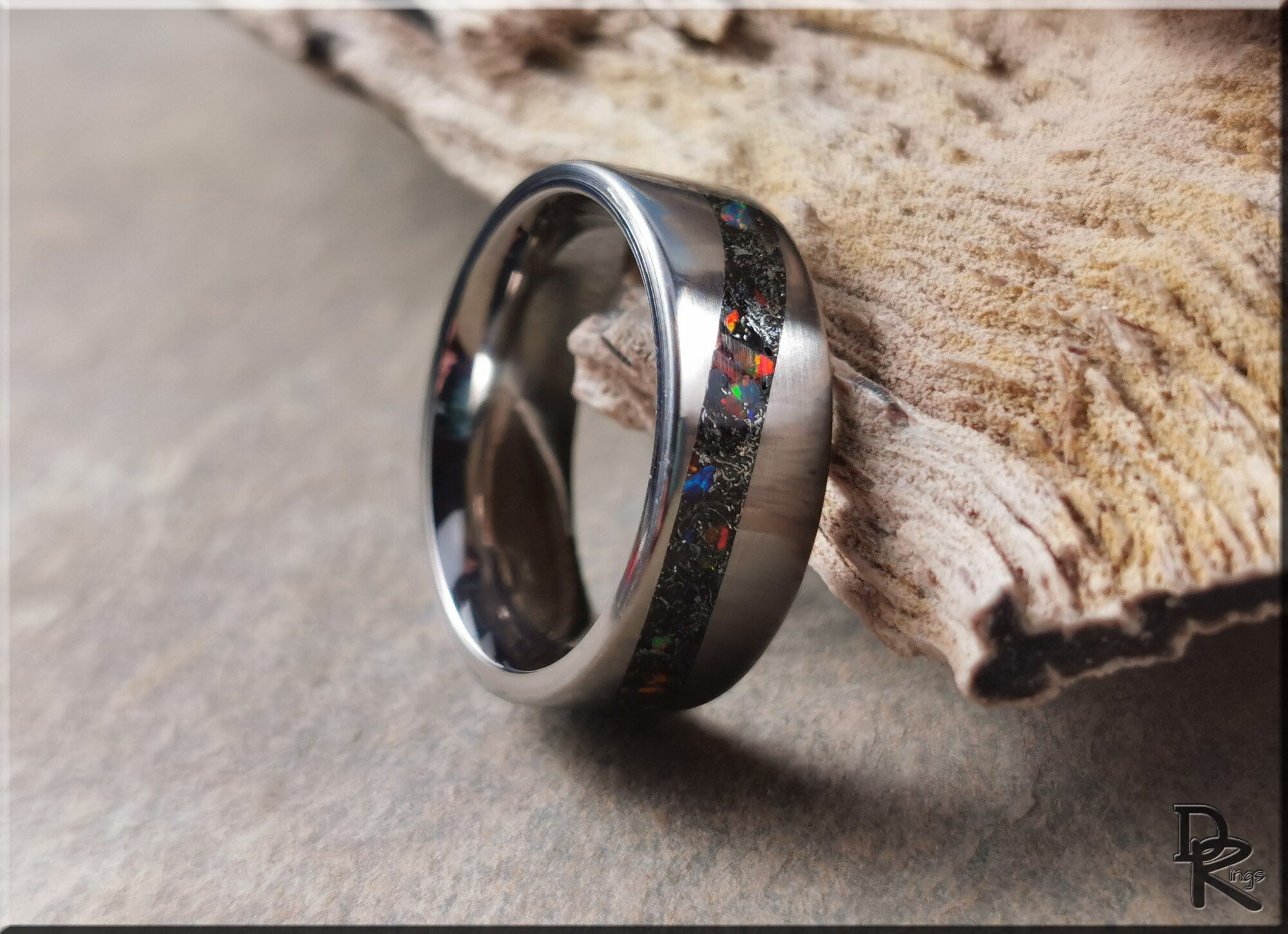 DR Rings titanium smart ring with black opal inlay resting on a textured wooden surface