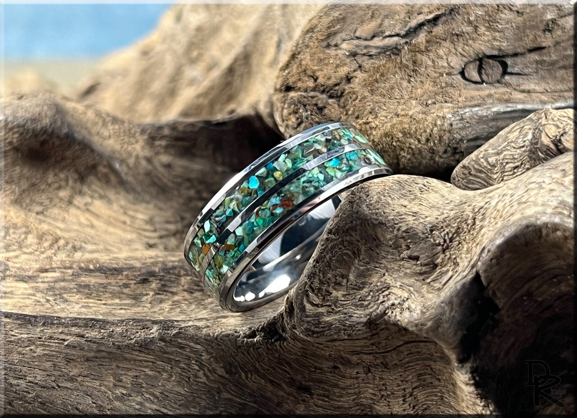 Tungsten carbide ring with two inlays featuring green and blue stone accents on wood background