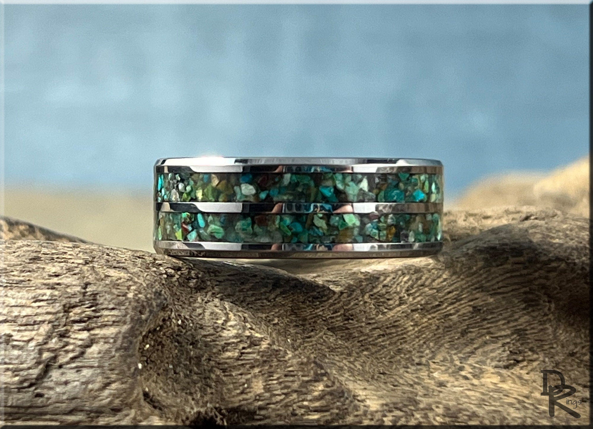 Tungsten carbide ring with two inlays featuring green and blue abalone shell design on wood background