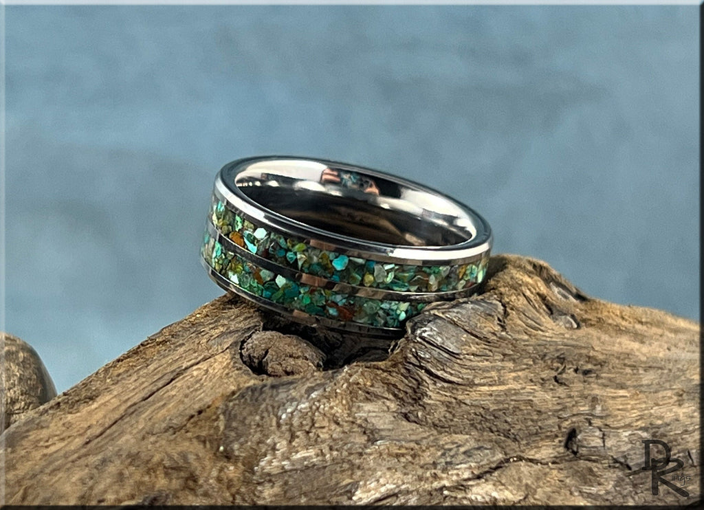 Tungsten carbide ring with two inlays featuring green and blue stone details on wooden surface by DR Rings
