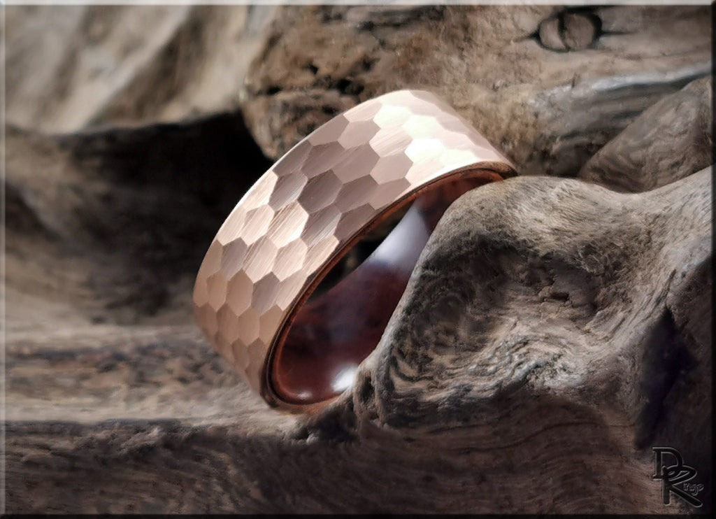 Hammered rose gold tungsten ring with wood liner displayed on textured wood surface by DR Rings