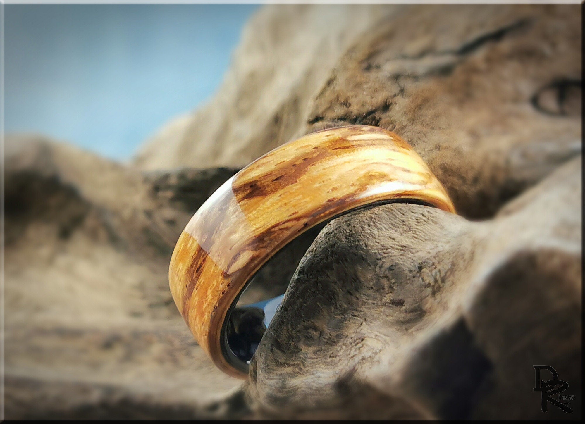 Wood ring on ceramic core with natural wood grain finish resting on textured driftwood