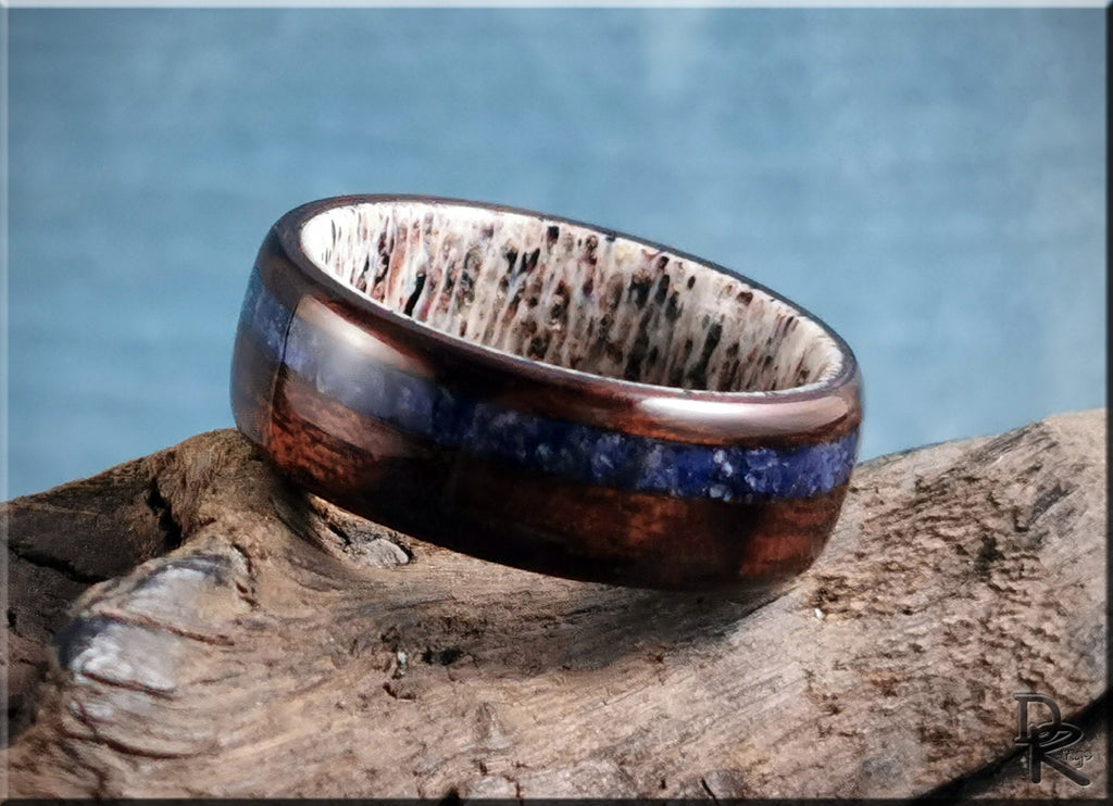 Wood ring with inlay featuring dark wood and blue stone detail on a rustic wooden surface