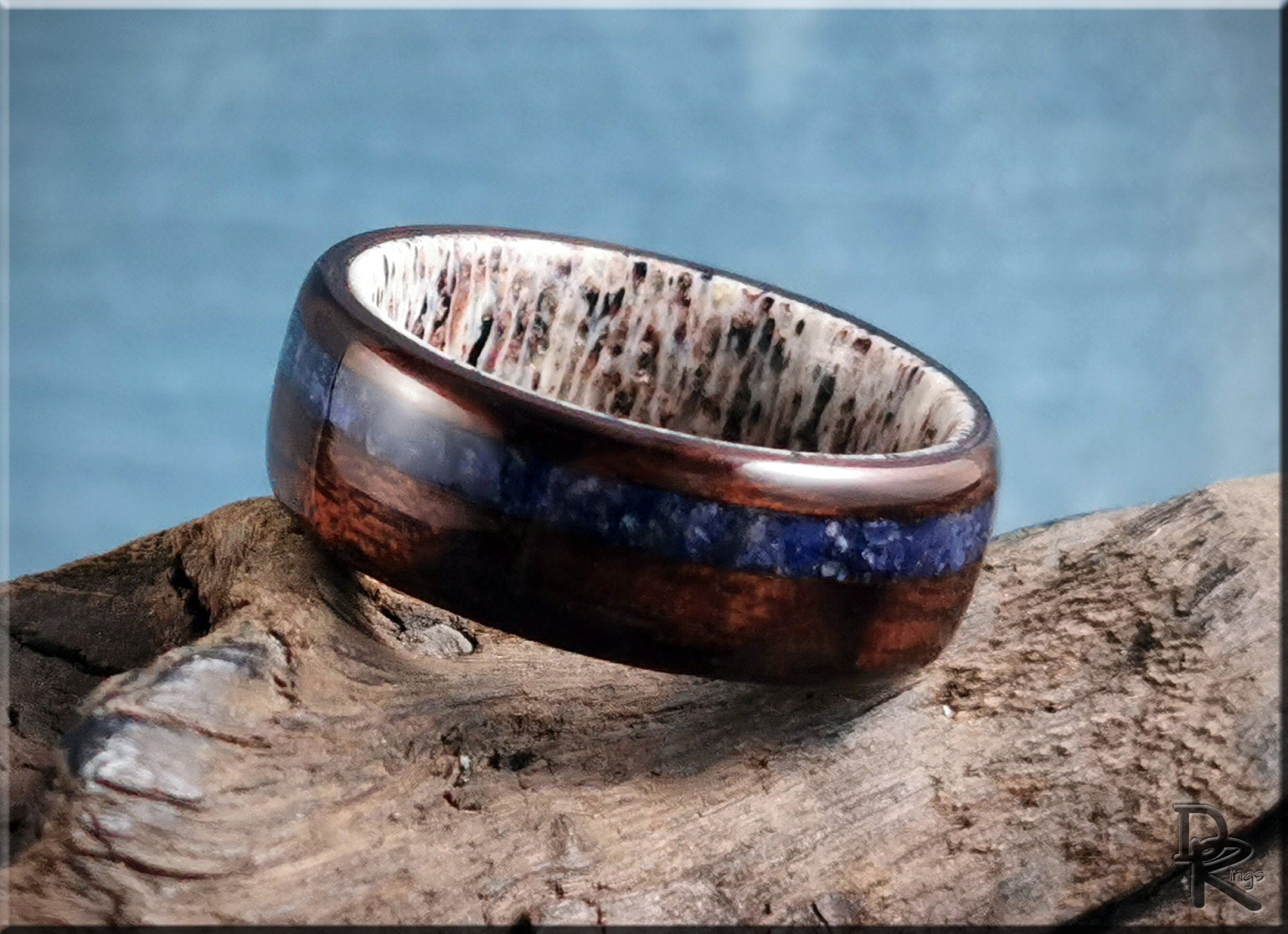 Wood ring with inlay featuring dark wood and blue stone detail on a rustic wooden surface
