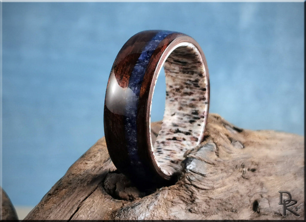 Wood ring with inlay featuring dark brown wood and blue stone on a textured wooden surface
