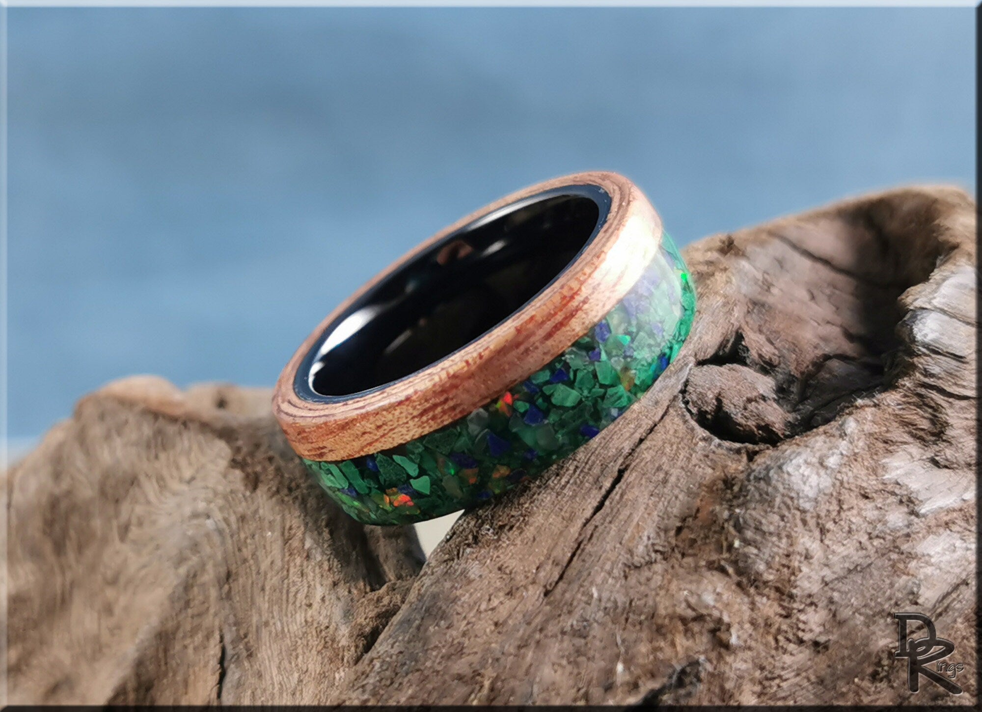 Wood ring with malachite inlay and black interior resting on natural wood by DR Rings
