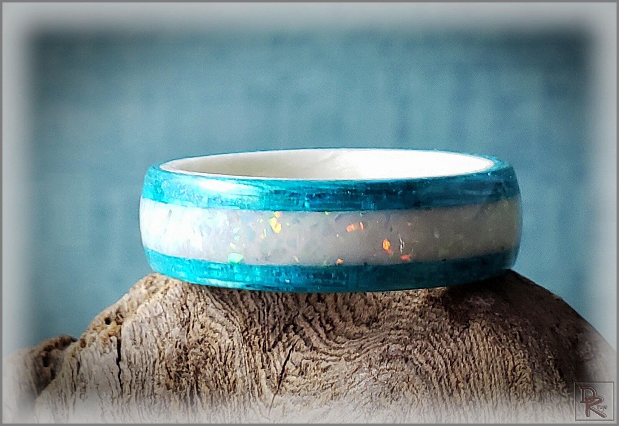 Blue wood ring with opal inlay featuring iridescent white center on textured wood background