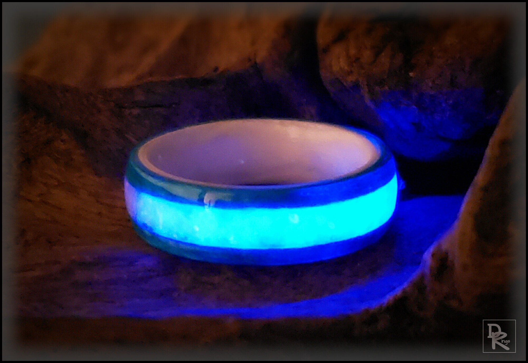 Wood ring with opal inlay glowing bright blue on a rustic wooden surface by DR Rings
