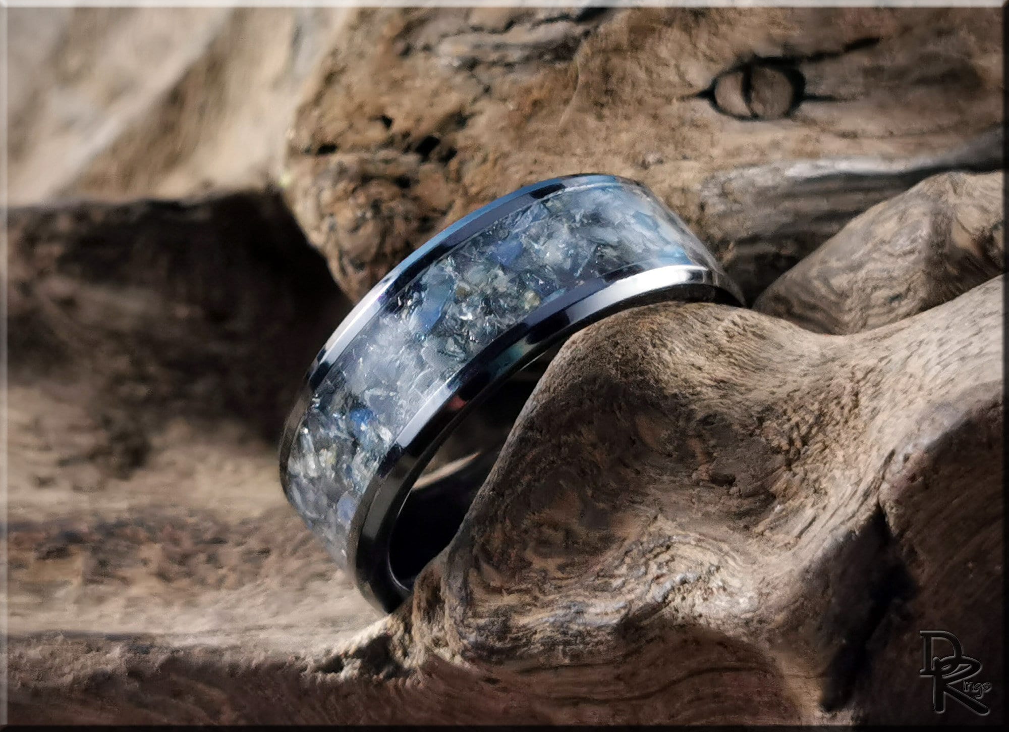DR Rings black ceramic ring with inlay featuring a unique blue and gray stone design on rustic wood background