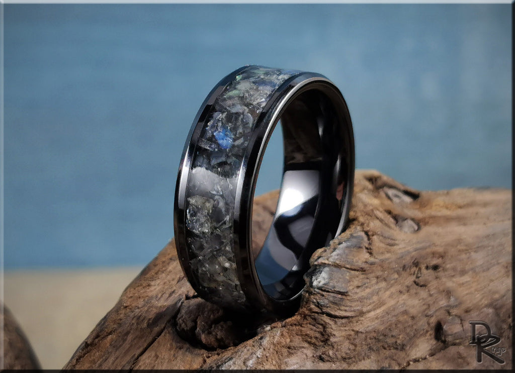 Black ceramic ring with inlay featuring a textured dark stone design on rustic wood background