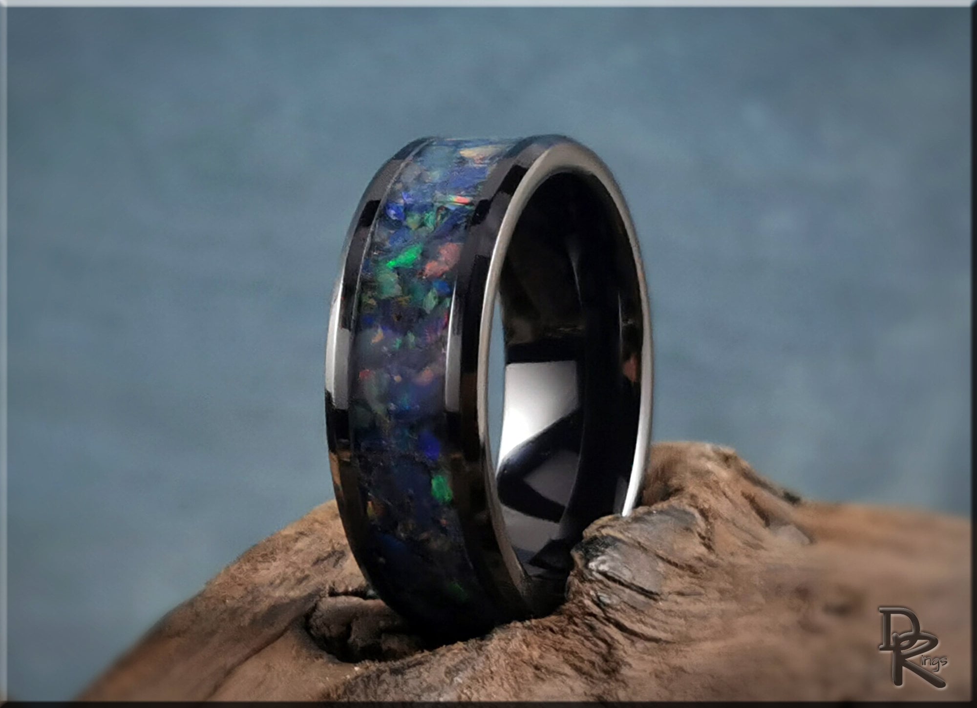 Black ceramic ring with opal inlay showcasing vibrant colors on a rustic wooden surface