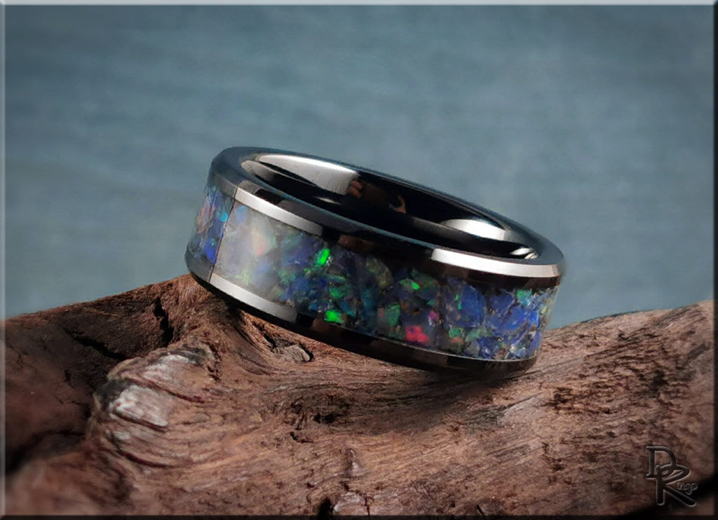 Black ceramic ring with opal inlay showcasing vibrant blue and green colors on rustic wood surface