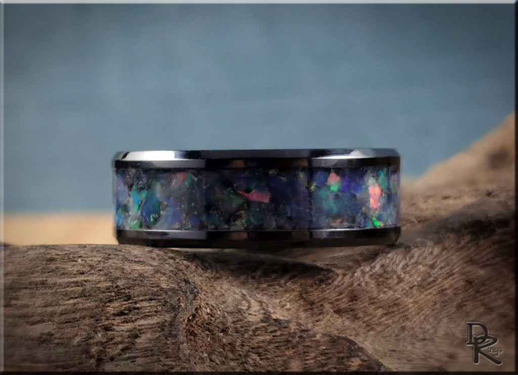 Black ceramic ring with opal inlay featuring multicolored iridescent stones on wood surface