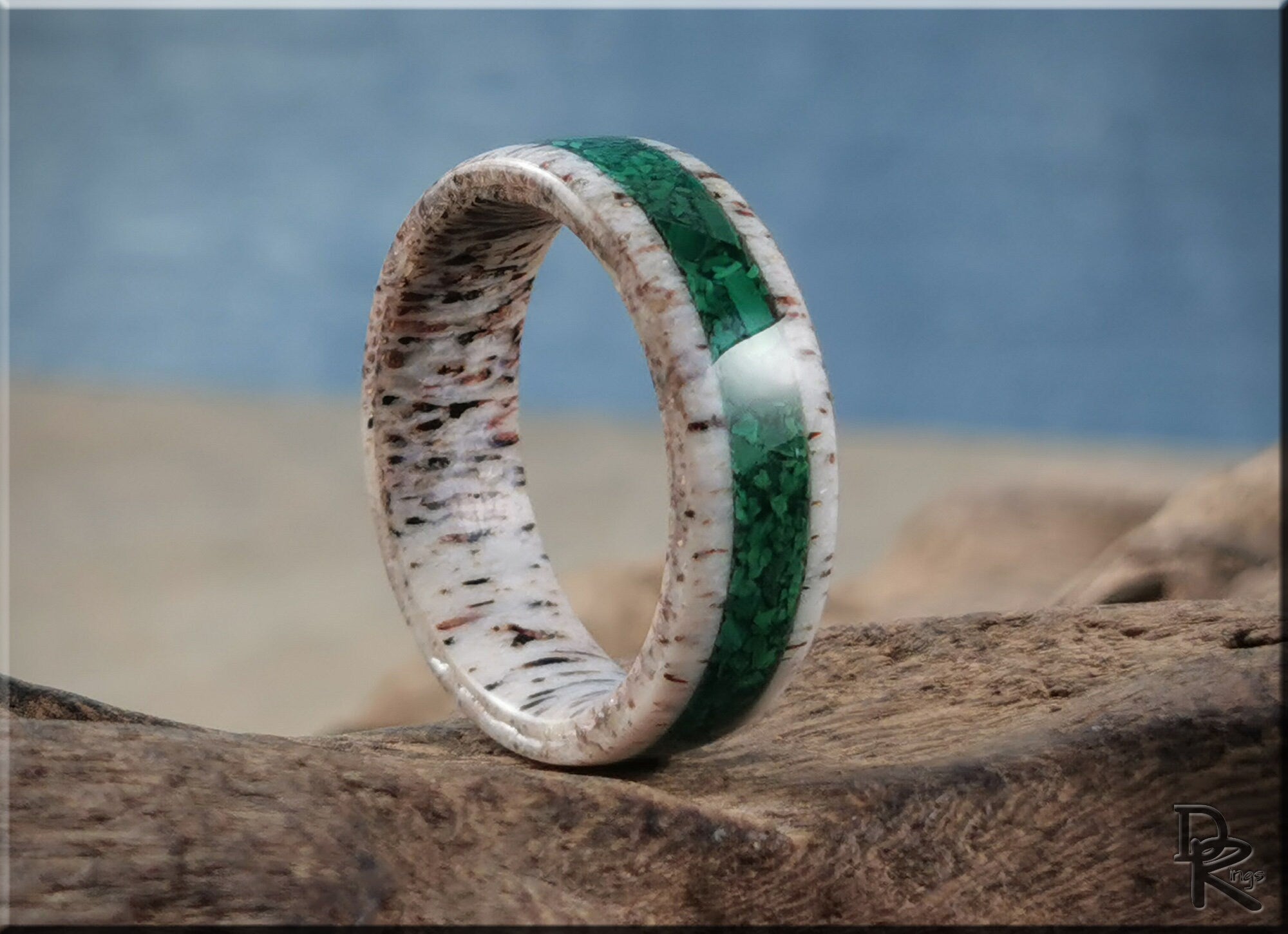 DR Rings antler ring with green inlay and natural wood texture resting on a rock outdoors