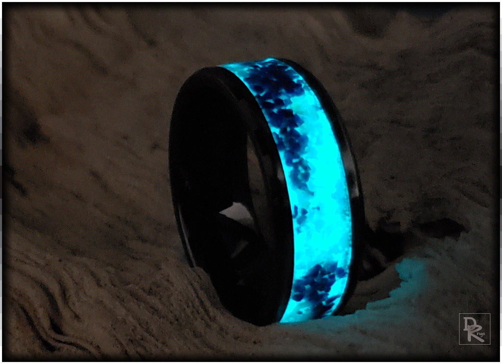 Black ceramic ring with glow inlay emitting bright blue light on a textured surface