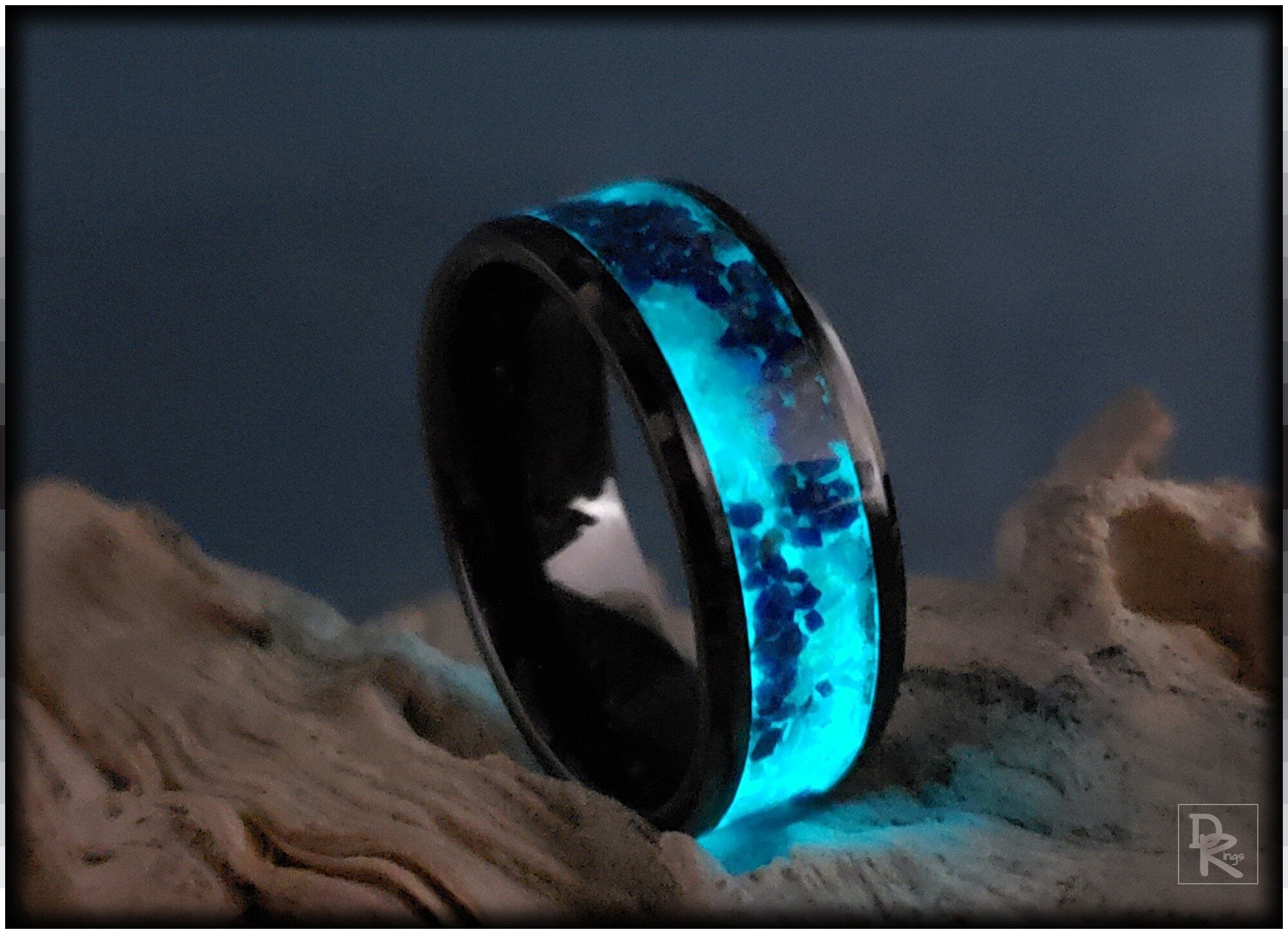 Ceramic ring with glow inlay glowing blue in the dark on a textured surface by DR Rings