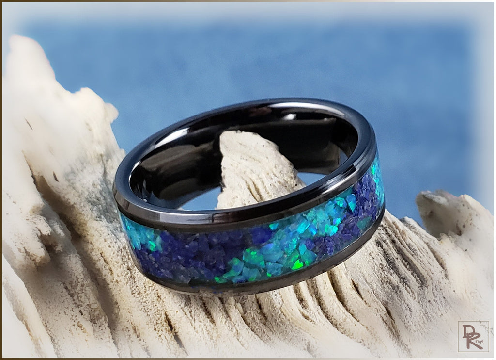 Black ceramic ring with glow inlay featuring vibrant blue and green tones on a textured surface