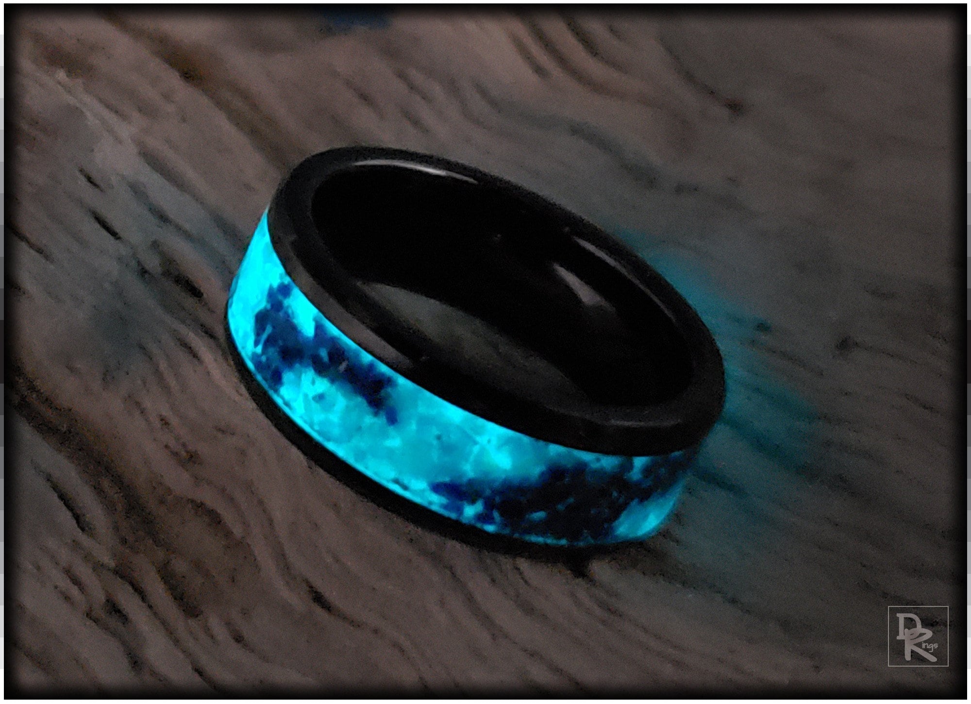 DR Rings ceramic ring with glow inlay glowing blue on a textured surface