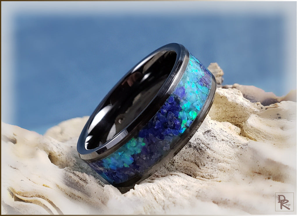 Ceramic ring with glow inlay featuring vibrant blue and green opal design on sandy background