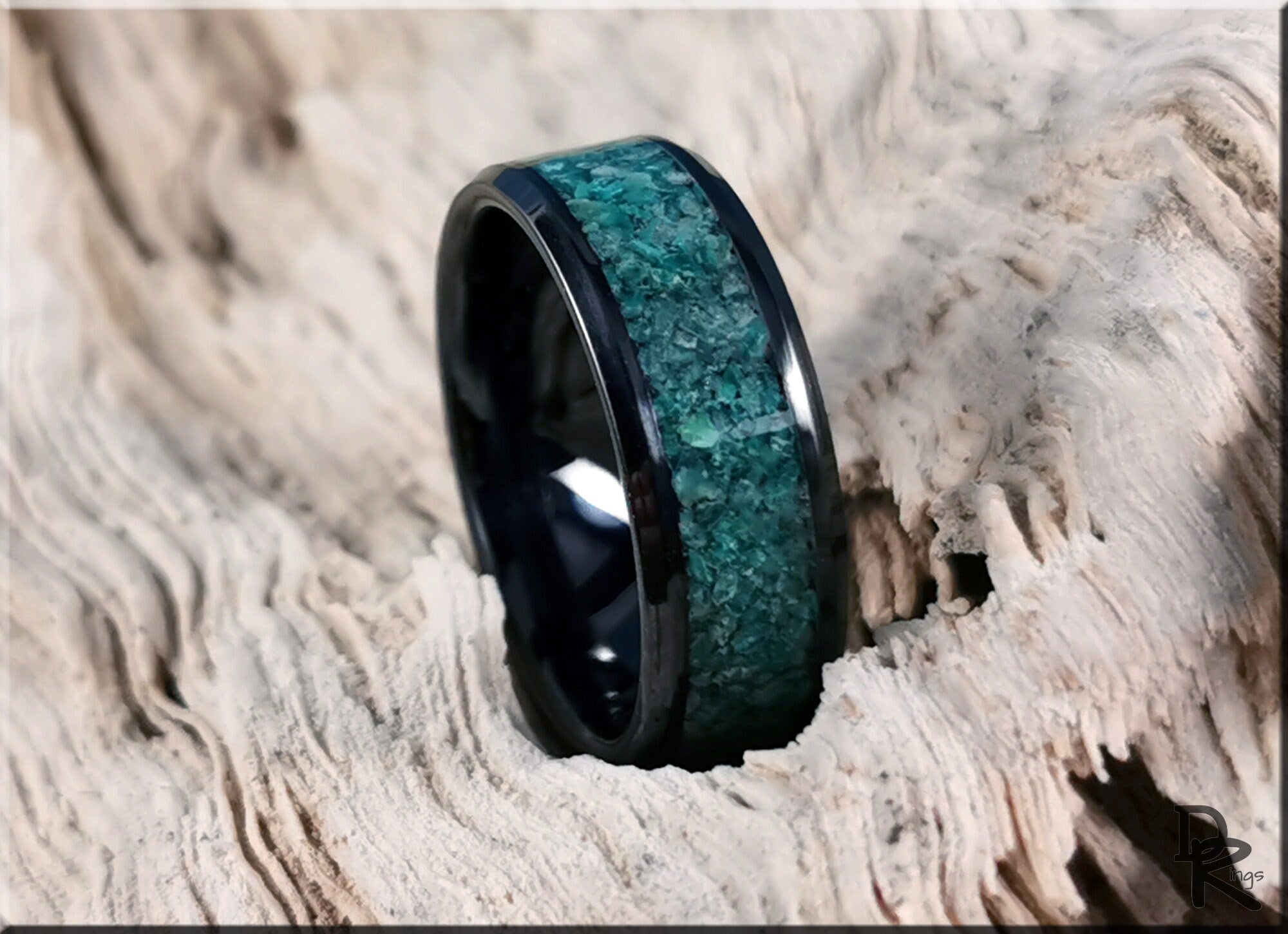Black ceramic ring with inlay featuring a textured green stone design on a rustic wooden surface