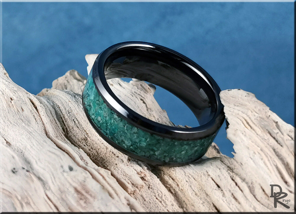 Black ceramic ring with inlay of crushed turquoise stones displayed on driftwood background