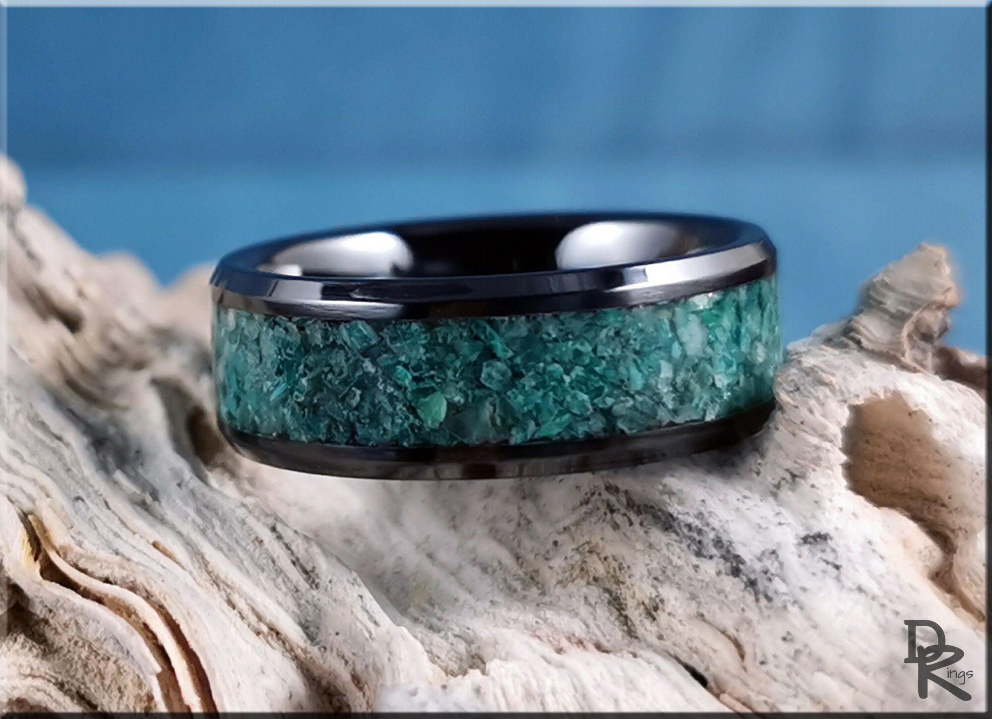 Black ceramic ring with inlay featuring green stone texture on a natural wood background