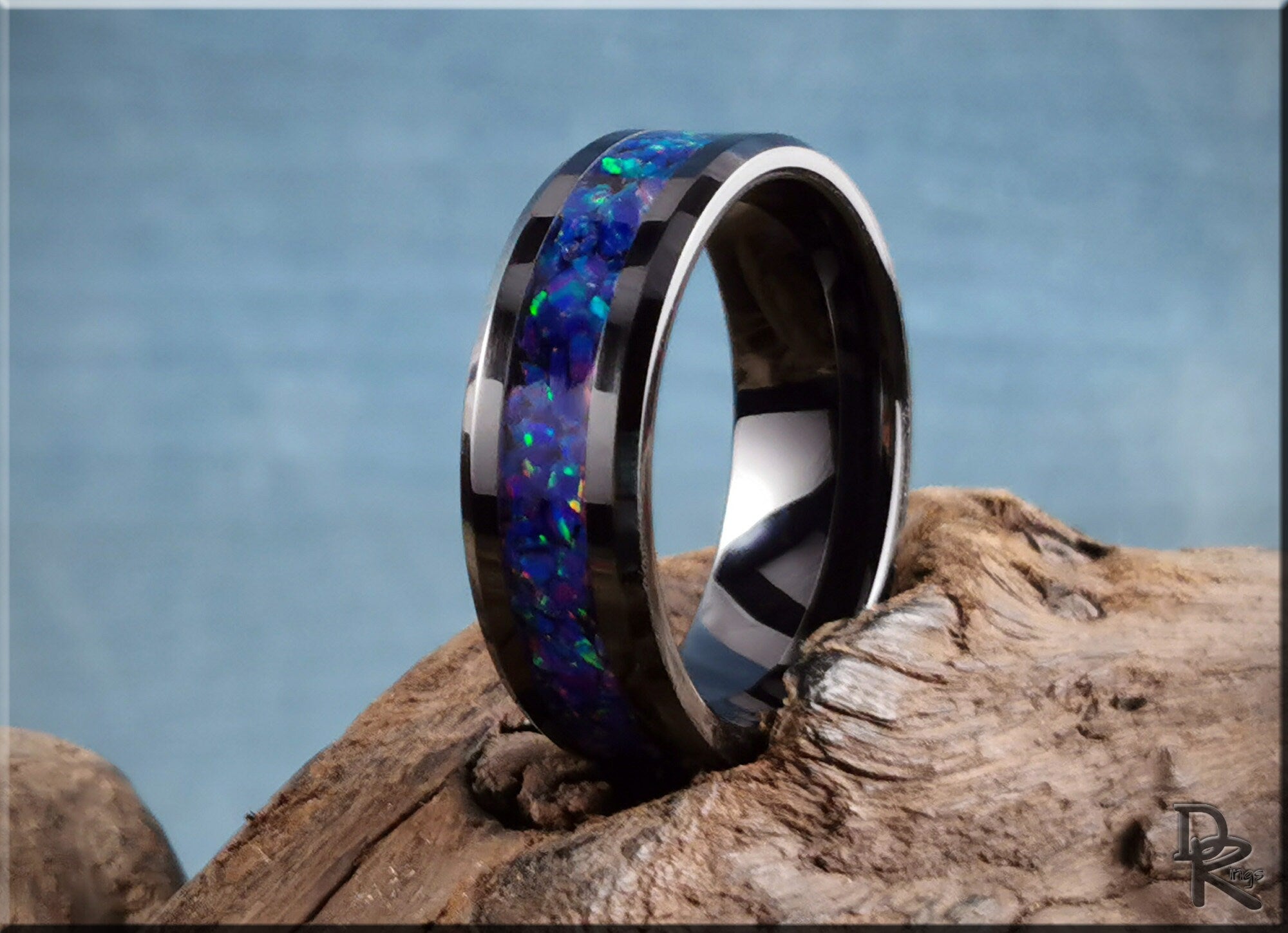 DR Rings ceramic ring with opal inlay featuring vibrant blue and green hues on rustic wood background