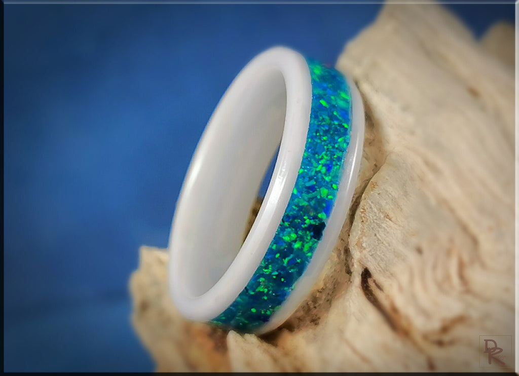 White ceramic ring with opal inlay featuring vibrant blue and green colors on a natural wooden surface