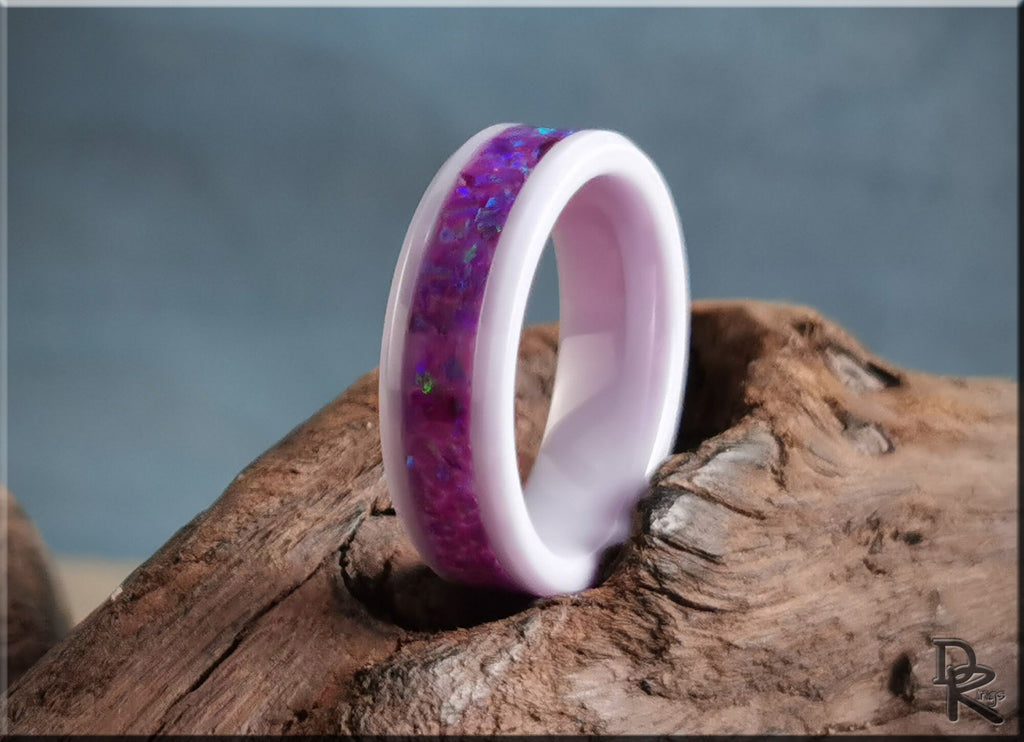 White ceramic ring with opal purple inlay displayed on rustic wood background by DR Rings
