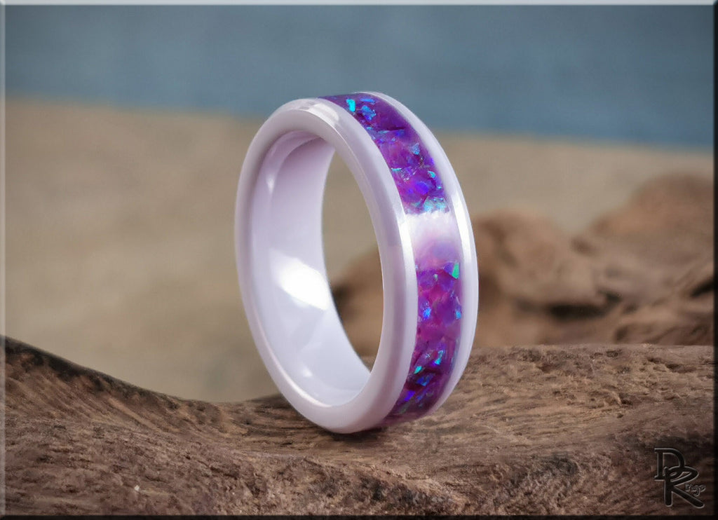 White ceramic ring with opal inlay featuring vibrant purple and blue colors on rustic background