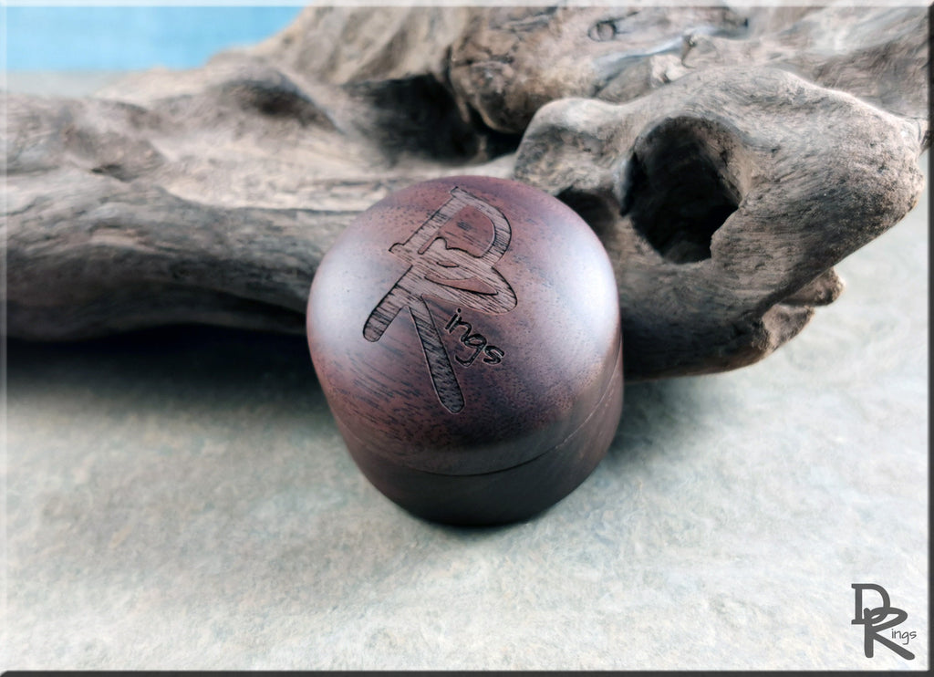 DR Rings walnut ring box with engraved logo displayed on textured surface and decorative driftwood